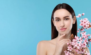 Güzel bir kadın, pürüzsüz bir ten ve açık mavi arka planda çiçekler. Metin için boşluk