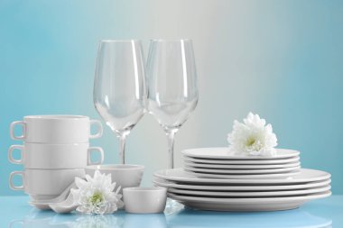 Açık mavi masada bir sürü temiz bulaşık, çiçek ve bardak var.