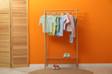 Farklı şık kadın kıyafetleri, ayakkabıları ve turuncu duvarın yanındaki ahşap perdeyle dizilin.