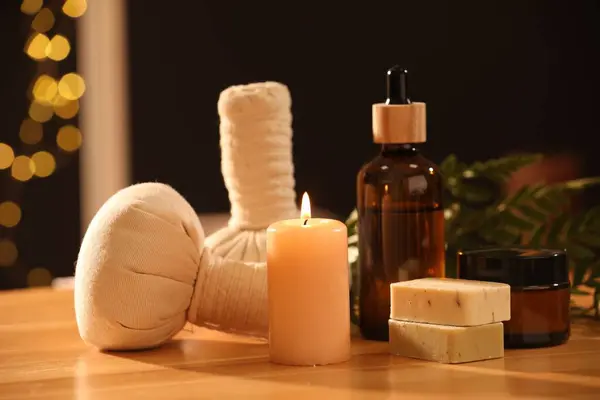 Spa composition. Cosmetic products, herbal bags and burning candle on wooden table
