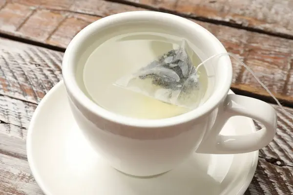 Tea bag in cup with hot water on wooden rustic table, closeup