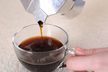 Moka pot 'tan açık dokulu masada cam fincana aromatik kahve döken kadın, yakın çekim.
