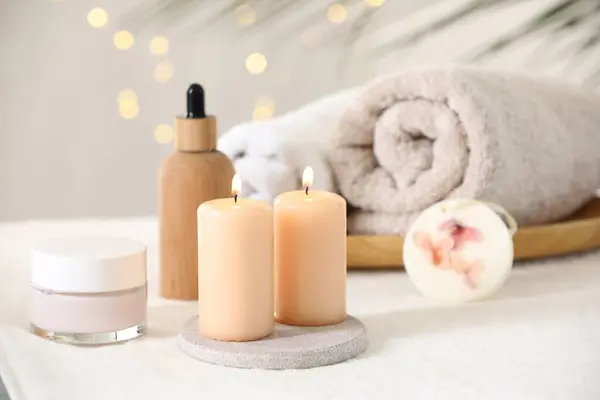 Spa composition. Burning candles and personal care products on soft white surface