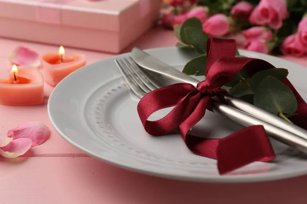 Place setting with roses and candles on pink wooden table, closeup. Romantic dinner