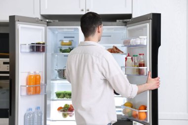 Buzdolabının yanında bir adam var. Mutfakta, arka tarafta.