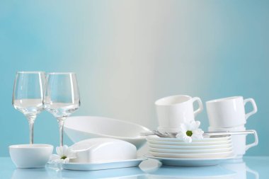 Açık mavi masada bir sürü temiz bulaşık takımı, çatal bıçak, çiçek ve bardak.