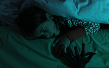 Çocukluk fobisi. Korkmuş kız yatağın altındaki canavara bakıyor, yakın plan.