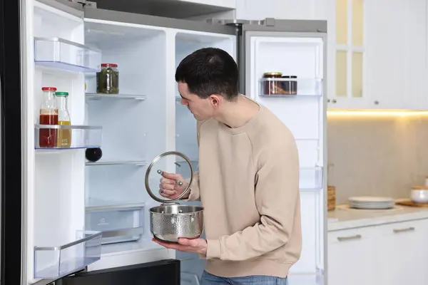 Man with pot near empty refrigerator in kitchen