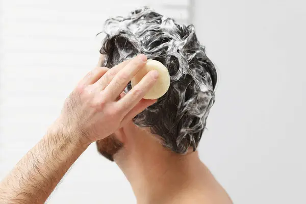 Man washing his hair with solid shampoo bar in shower, closeup