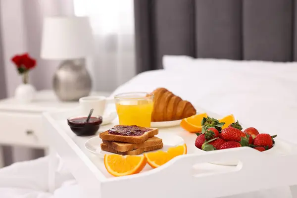Tray with delicious breakfast on bed in room, closeup.