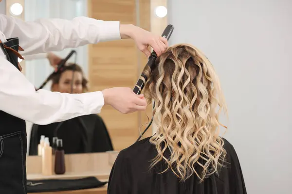 Hair styling. Hairdresser curling woman\'s hair in salon, closeup