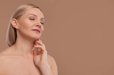 Güzel bir kadın bej arka planda boynuna dokunuyor, mesaj için boşluk var.