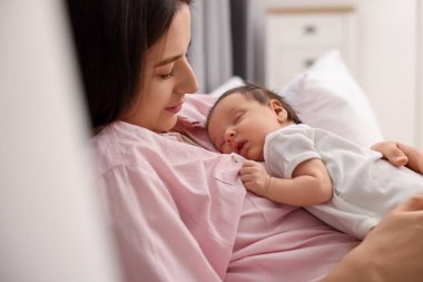 Anne, uyuyan yeni doğmuş bebeğiyle evde yatıyor.