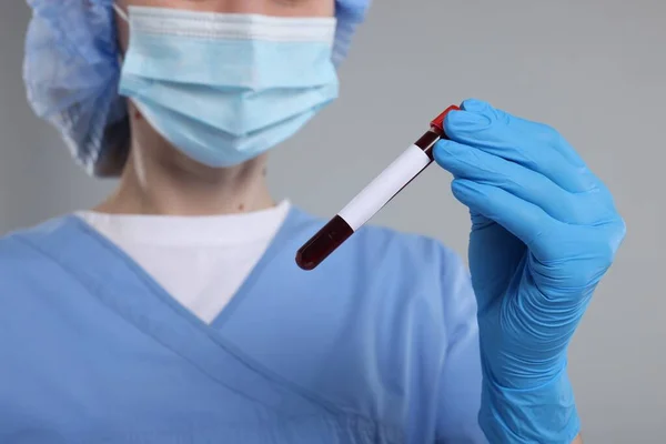Laboratory testing. Doctor with blood sample in tube on light grey background, closeup