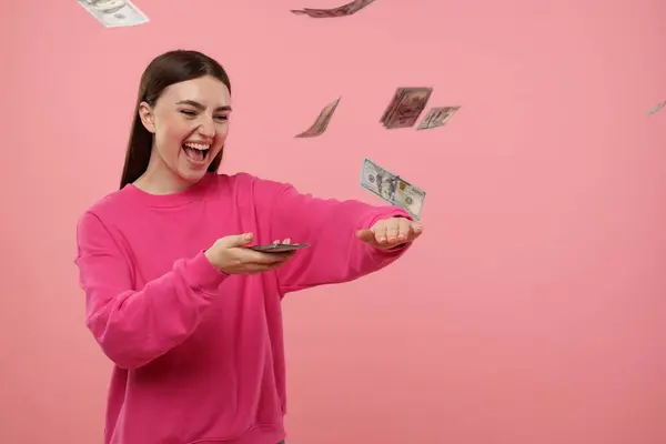 Happy woman throwing money on pink background, space for text