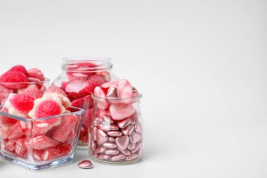 Cam kavanozlarda farklı lezzetli pembe şekerler ve beyaz arka planda kaseler, metin için yer.