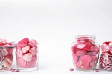 Cam kavanozlarda farklı lezzetli pembe şekerler ve beyaz arka planda kaseler, metin için yer.