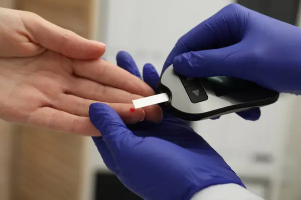 Diabetes. Doctor checking patient\'s blood sugar level with glucometer in clinic, closeup