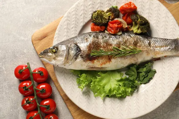 Delicious baked fish and vegetables on light grey table, top view