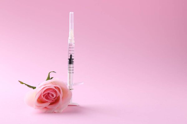 Cosmetology. Medical syringe and rose flower on pink background, space for text