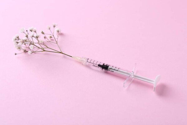 Cosmetology. Medical syringe and gypsophila on pink background