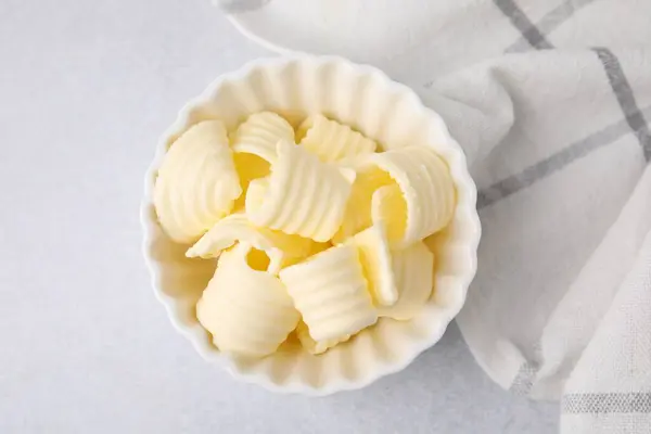 Tasty butter curls in bowl on light grey table, top view