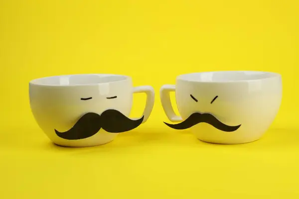 Men\'s faces made of cups, fake mustaches on yellow background