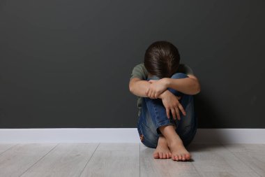 Çocuk istismarı. Üzgün kız gri duvarın yanında oturuyor, mesaj için yer var.