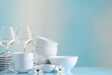 Açık mavi masada bir sürü temiz bulaşık takımı, çiçekler ve bardaklar. Metin için boşluk