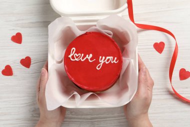 Beyaz ahşap masada elinde Bento kekiyle paket servisi yapan bir kadın. Sevgililer Günü sürprizi