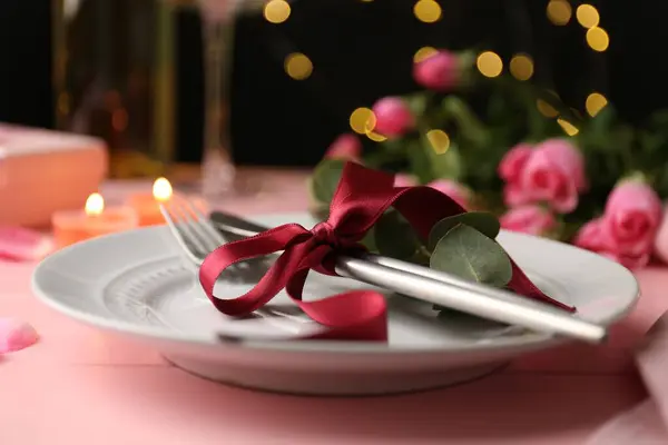 Place setting with roses and candles on pink table, closeup. Romantic dinner