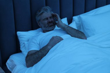 Yetişkin bir adam gece yatağında baş ağrısı çekiyor.