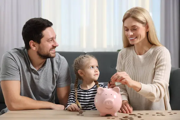 ファミリー予算 小さな女の子と彼女の両親は自宅でブタバンにコインを入れて — ストック写真
