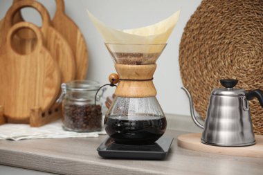 Damlalı kahve yapıyorum. Cam kimya kahve makinesi, kağıt filtresi, fasulye kavanozu ve mutfak tezgahındaki ahşap su ısıtıcısı.