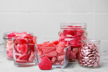 Cam kavanozlarda farklı lezzetli şekerler ve beyaz mermer masada kaseler.