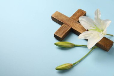 Ahşap haç ve açık mavi arka planda zambak çiçekleri, yazı için boşluk. Paskalya özellikleri