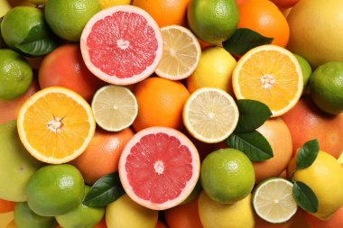 Different fresh citrus fruits and leaves as background, top view