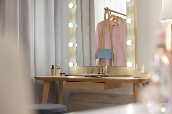 Stylish mirror with light bulbs and beauty products on wooden dressing table in makeup room