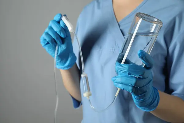 Nurse with IV infusion set on grey background, closeup