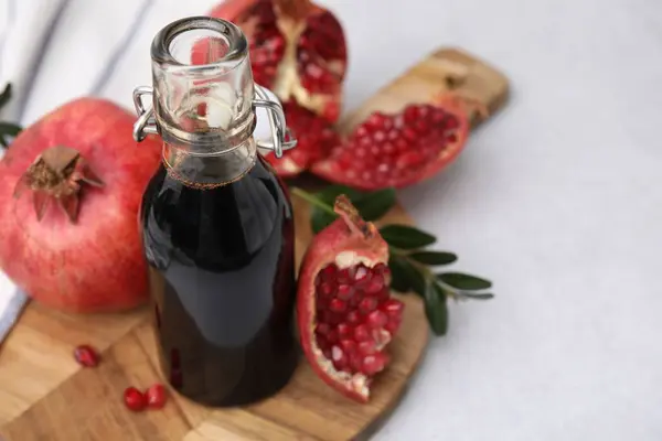 Tasty pomegranate sauce in bottle, branch and fruits on light table, closeup. Space for text