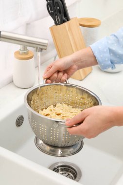 Lavabonun üstünde makarnayı durulayan kadın, yakın plan.