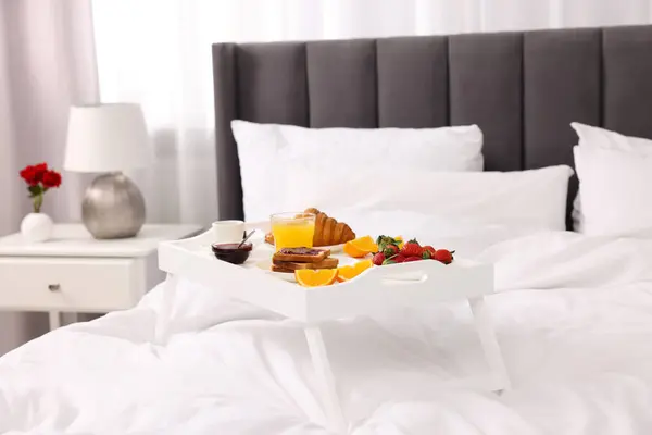 Tray with delicious breakfast on bed in room