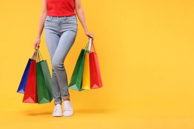 Sarı arka planda alışveriş torbaları olan kadın, yakın plan. Metin için boşluk