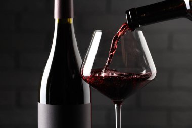 Kırmızı şarabı cama ve şişeleri tuğla duvara dökerek, yakın plan