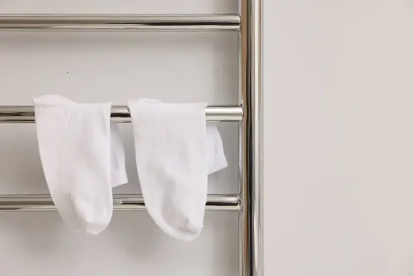 Heated towel rail with socks on white wall, closeup. Space for text