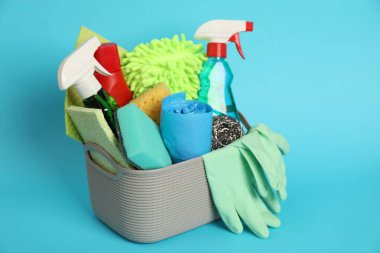 Açık mavi arka planda sepette farklı temizlik ürünleri