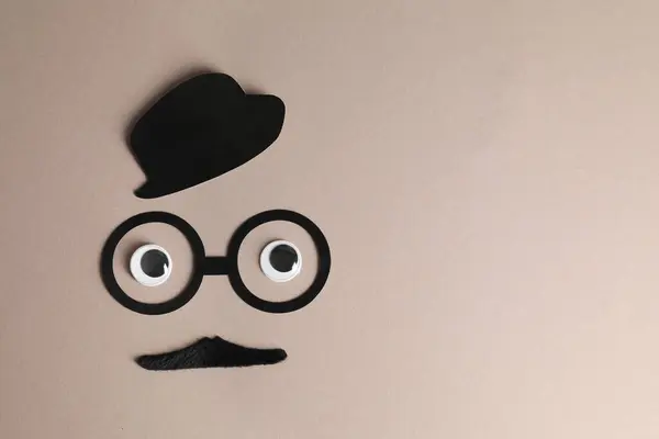 Man\'s face made of fake mustache, paper hat and glasses on grey background, top view. Space for text
