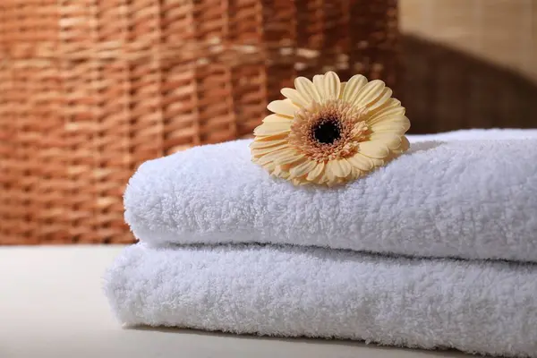 Stacked terry towels and flower on white table indoors, closeup. Space for text