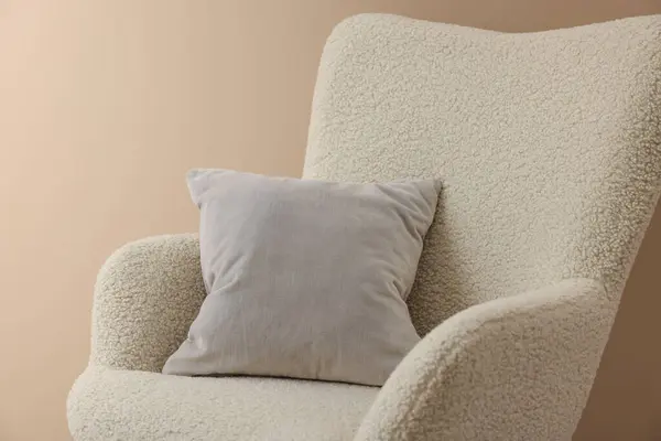 Soft grey pillow on armchair near beige wall