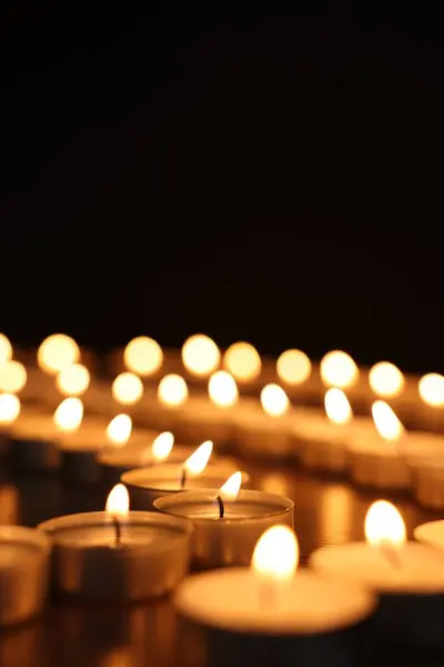 Burning candles on dark surface against black background